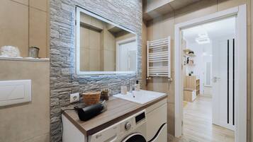 A modern bathroom with a stone accent wall, a sink, a mirror, and a washing machine.