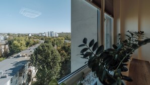 A room with a large window offering a view of a cityscape and greenery.