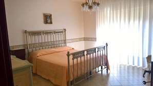 Un dormitori amb llit, una tauleta de nit, un armari, un penjó i una finestra amb cortines.