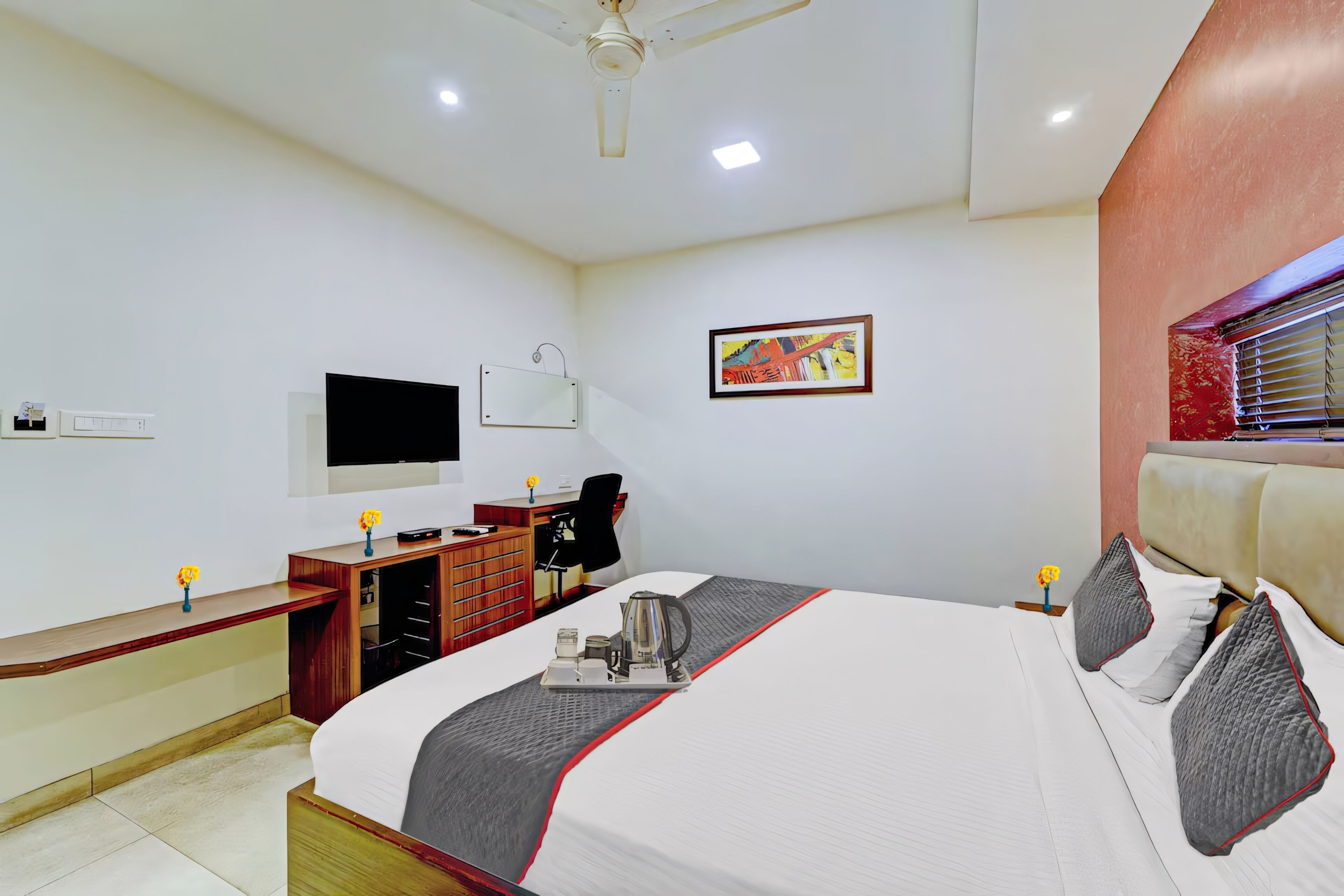 Ein Hotelzimmer mit Bett, Schreibtisch, Stuhl, Fernseher und einem Fenster mit Jalousien.