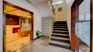 A modern hotel lobby with a glass door entrance, a staircase, and a reception desk. - RG Suites Royapettah (Chennai)