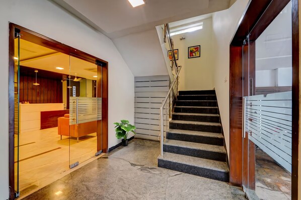 A modern hotel lobby with a glass door entrance, a staircase, and a reception desk. - RG Suites Royapettah (Chennai)