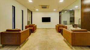 A conference room with a large flat-screen TV, brown leather sofas, and a marble floor. - RG Suites Royapettah (Chennai)