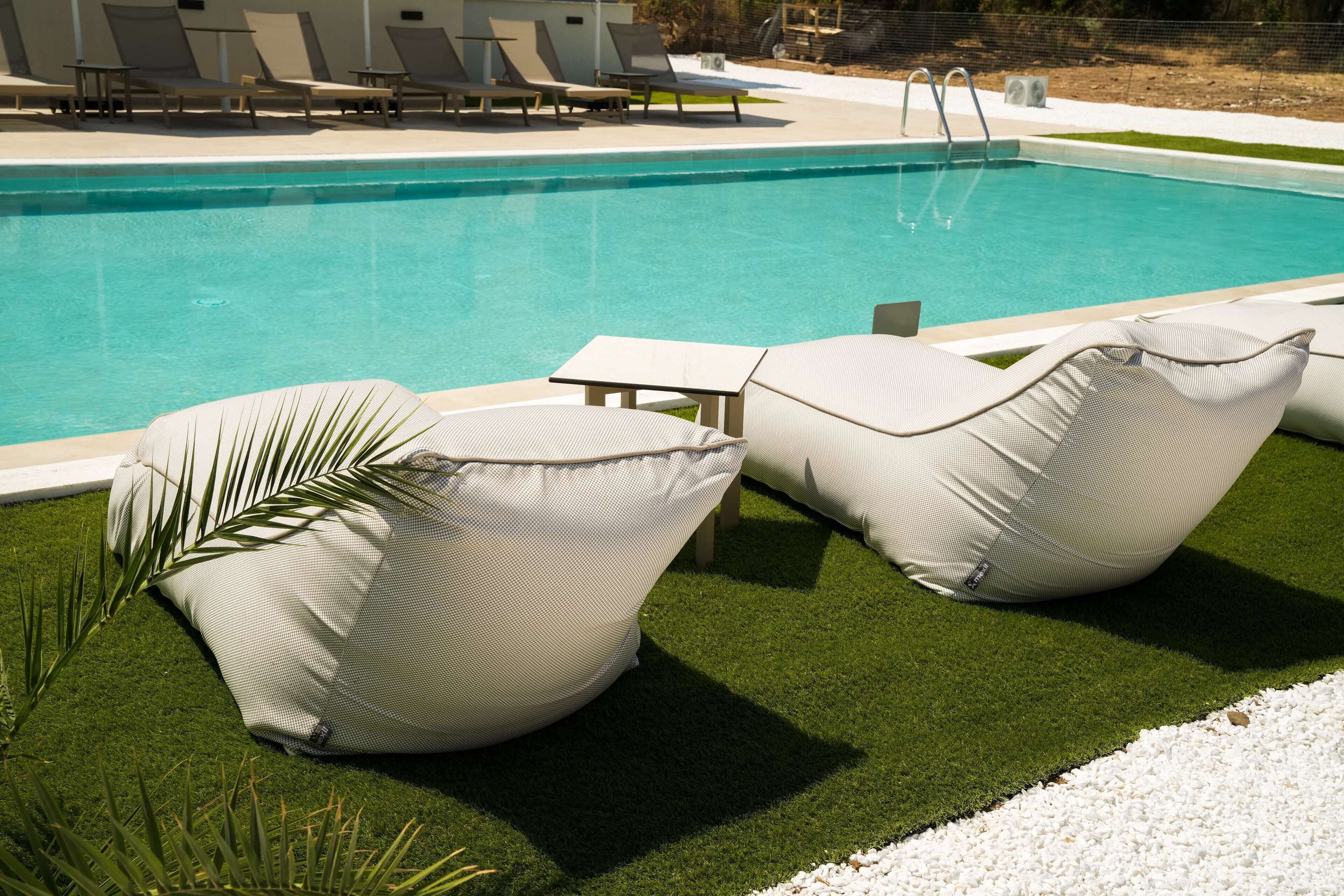 Un área junto a la piscina con sillones de descanso y una pequeña mesa.