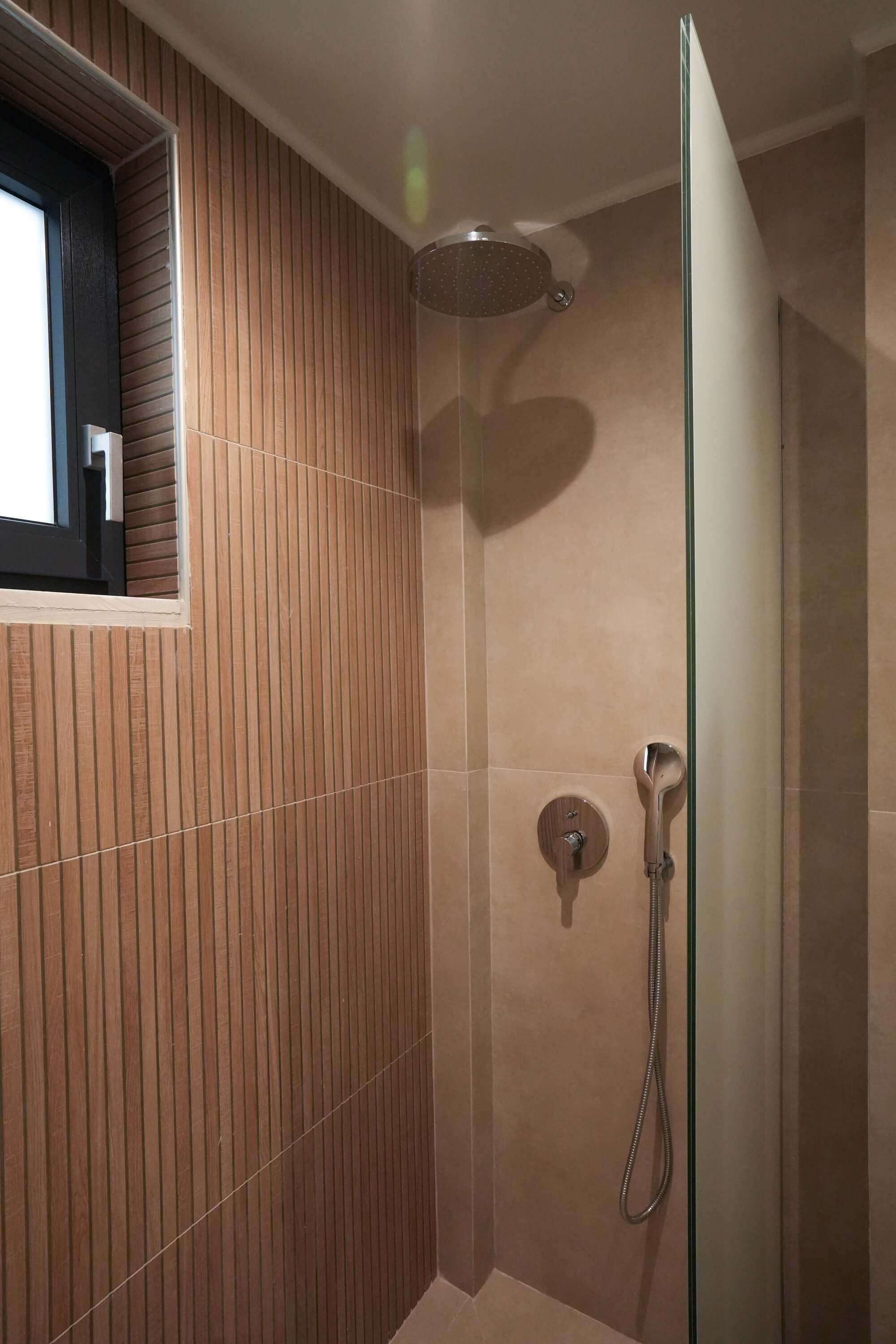 A shower with a glass door, wooden paneling on one wall, and a round showerhead.