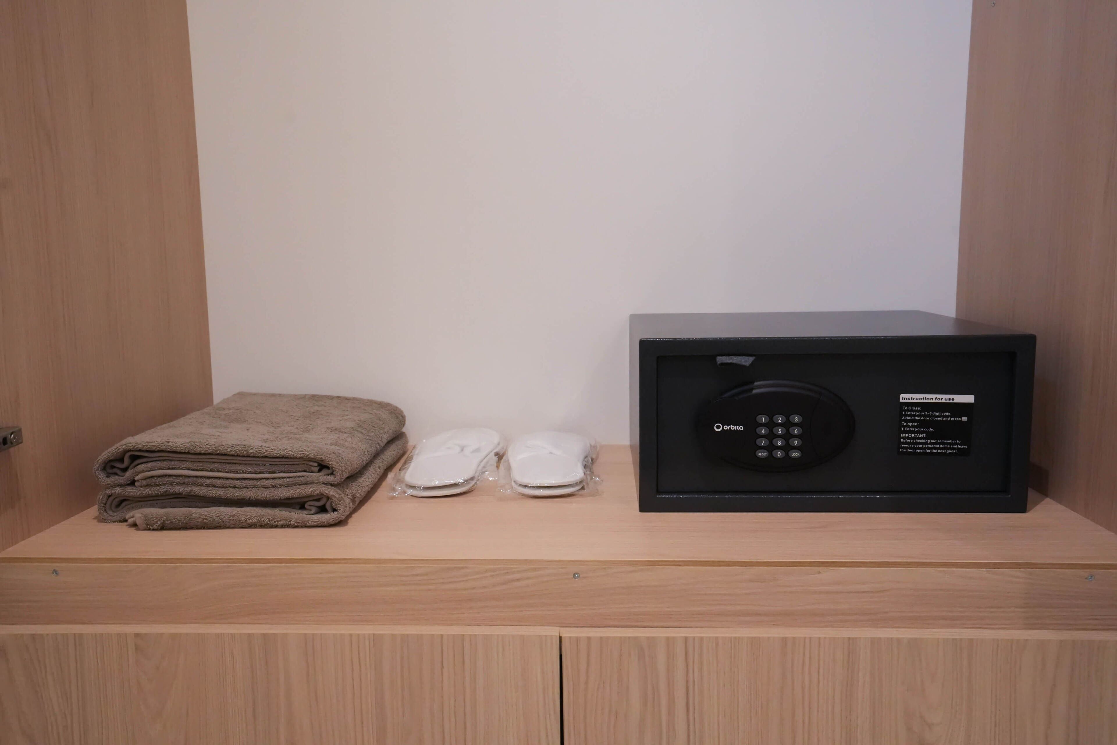 A wooden cabinet with a black safe, a folded towel, and two slippers.