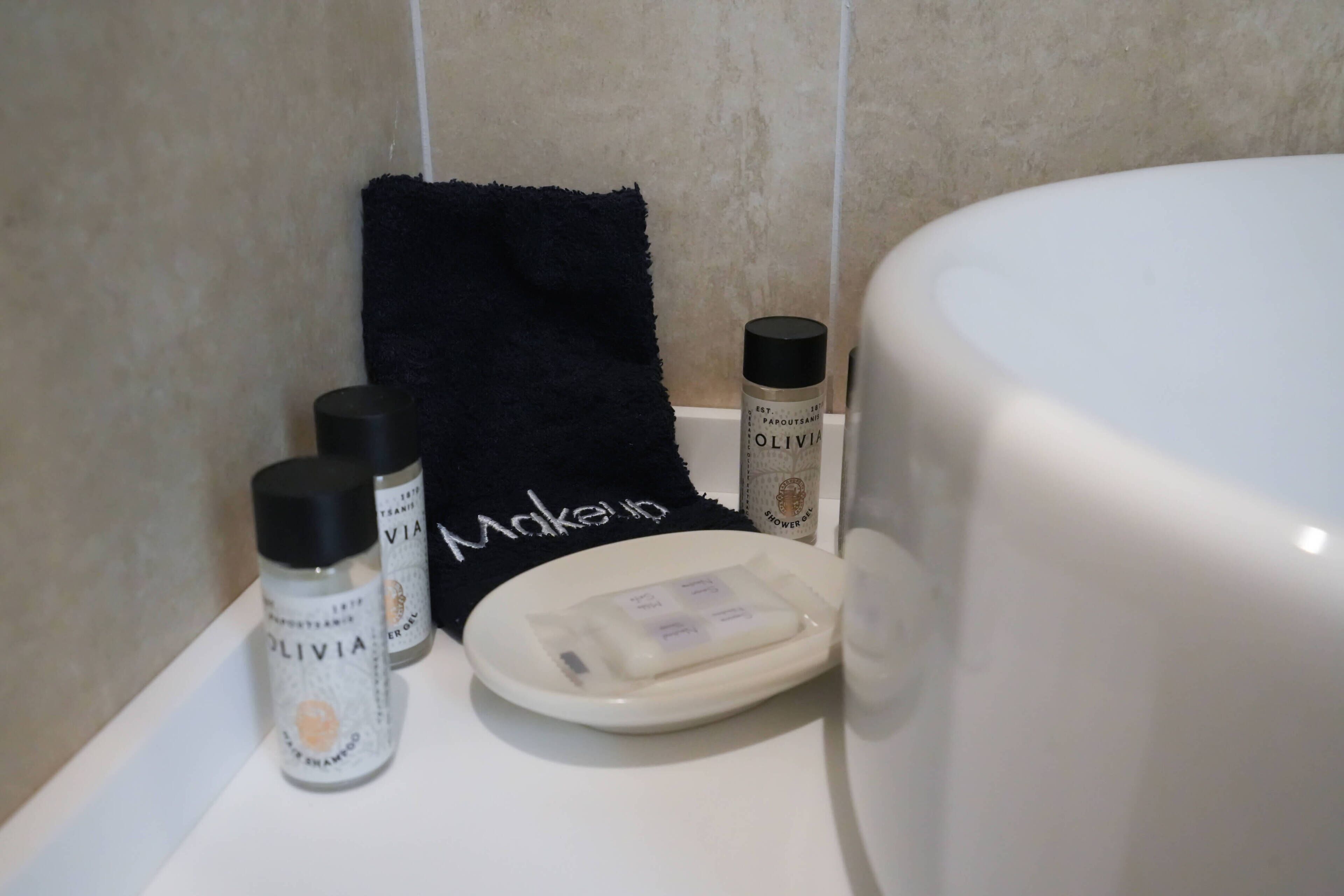 Un baño con una bañera blanca, una toalla negra y dos botellas de gel de ducha Olivia.