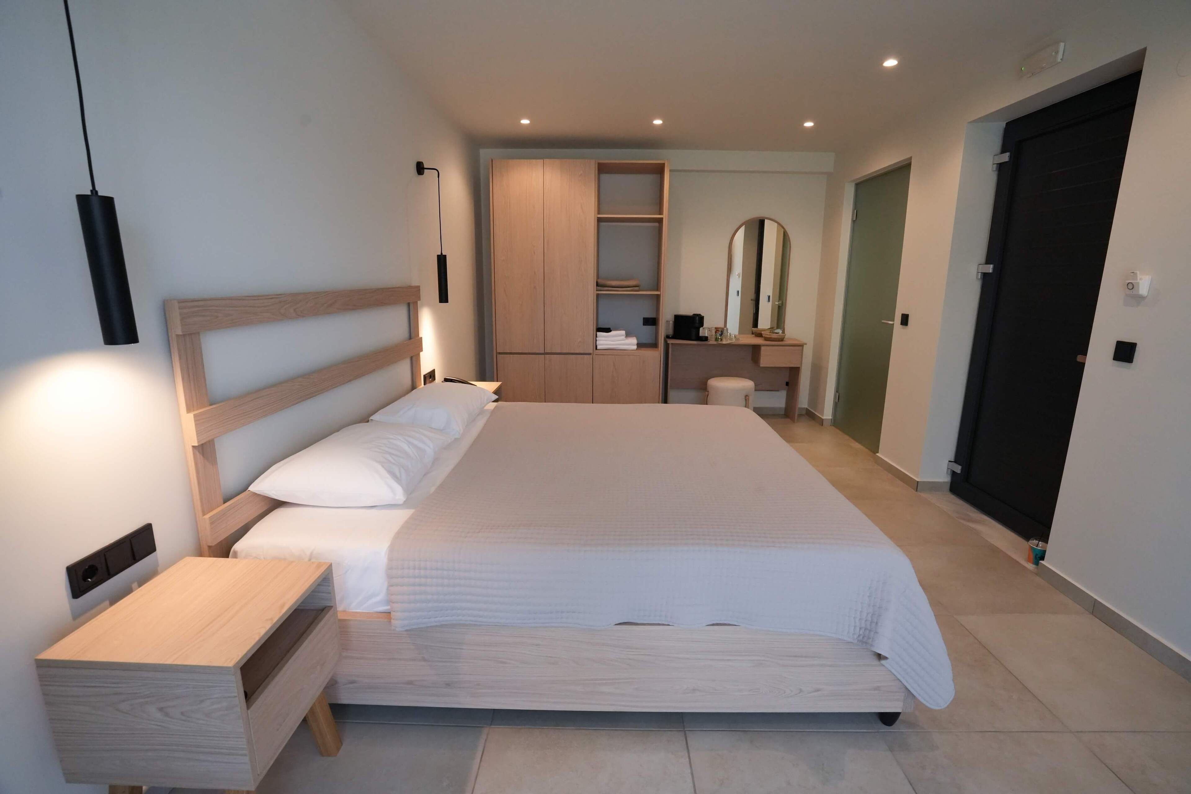 A modern bedroom with a large bed, bedside tables, a wardrobe, a mirror, and a door.