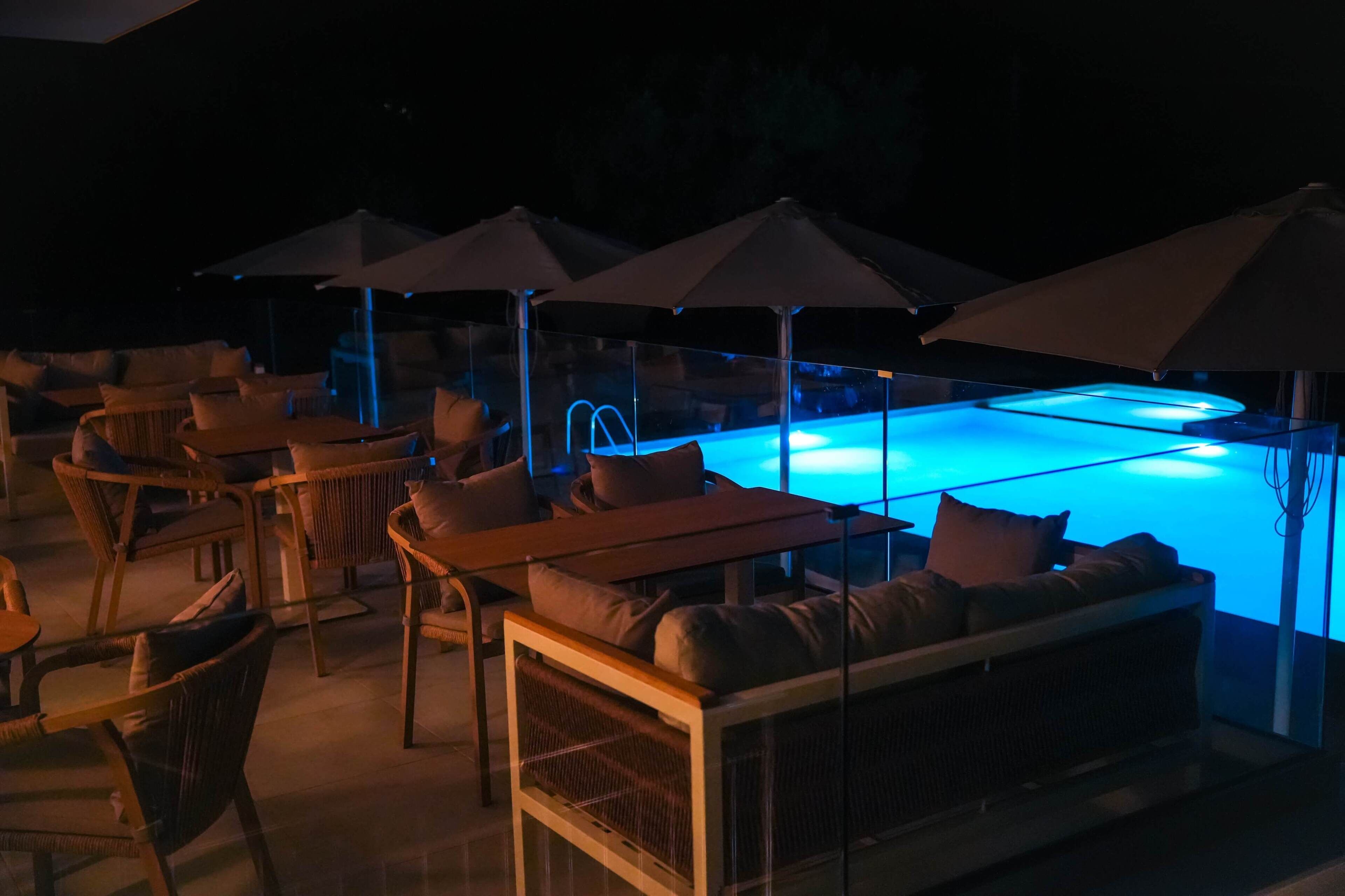 An outdoor pool area with lounge chairs and umbrellas, surrounded by glass walls.