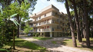 Een meerlaags appartementencomplex met balkons, omringd door bomen en een grindpad.