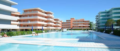 A swimming pool area with multiple hotel buildings in the background.