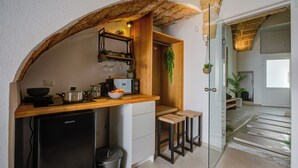Une cuisine compacte dotée d’un plan de travail en bois, d’un petit réfrigérateur et d’une porte en verre donnant sur un espace de vie avec un escalier.