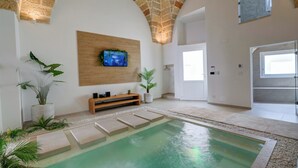 Un espace piscine intérieur moderne avec un plafond en pierre, un téléviseur fixé au mur et un banc en bois.
