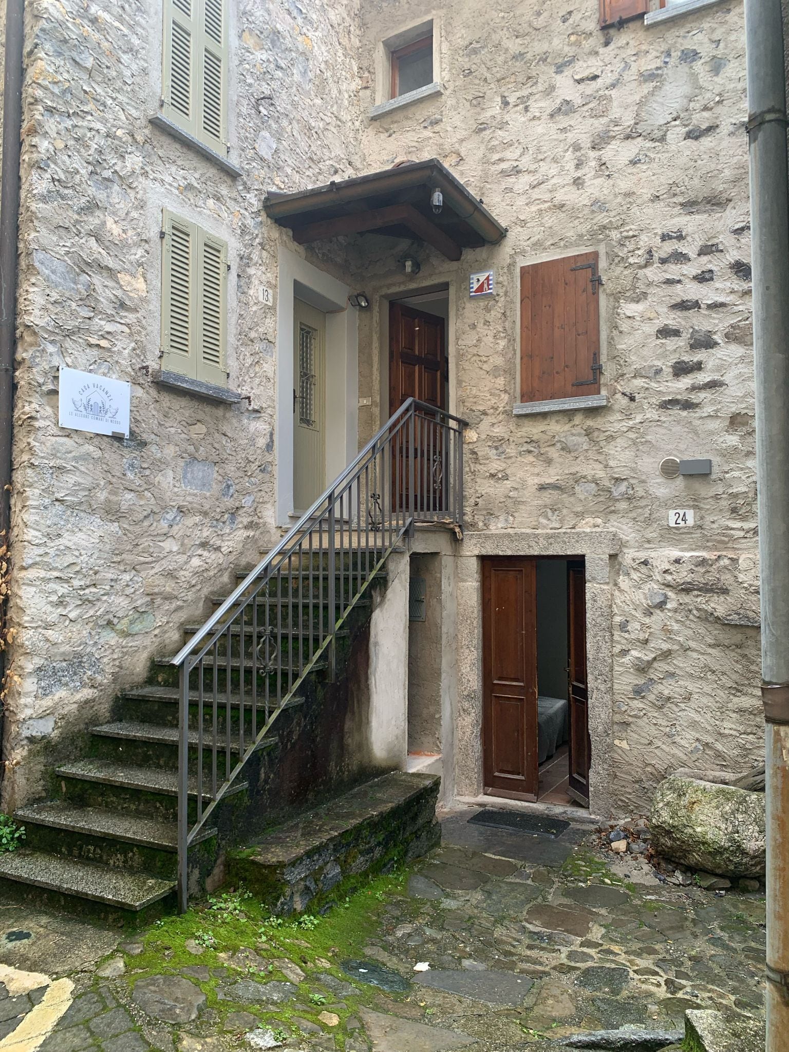 A stone building with a staircase leading to a wooden door, a small balcony, and a sign indicating a vacancy.