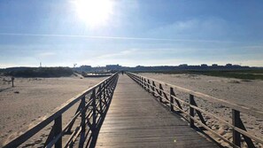 Un paseo marítimo de madera que lleva a una playa, bajo un cielo despejado.
