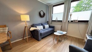 Un salon chaleureux avec un canapé gris, un plancher en bois, une petite table ronde et une lampe.