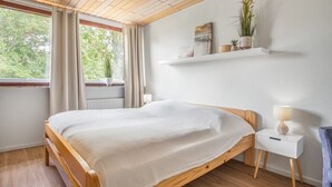 Une chambre à coucher avec un lit en bois, une table de chevet blanche, une lampe et une étagère avec des plantes.
