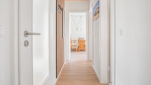 Un couloir doté d’un plancher en bois, de murs blancs et d’une porte avec une poignée argentée.