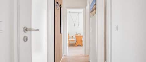 A hallway with a wooden floor, white walls, and a door with a silver handle.