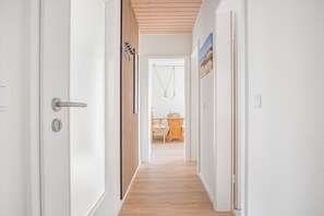 A hallway with a wooden floor, white walls, and a door with a silver handle. - Gemütliche Wohnung für 2 Gäste am Meer (Sankt Peter-Ording)