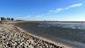 A beach with a rocky shoreline, a building with multiple balconies, and a clear blue sky. - Bright apartment at the Family Lagoon w/ balcony (Büsum)