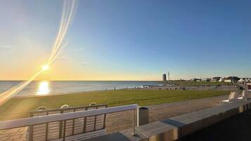 Eine Uferpromenade mit einer Bank, einem Geländer und Blick auf das Meer sowie Gebäude in der Ferne.