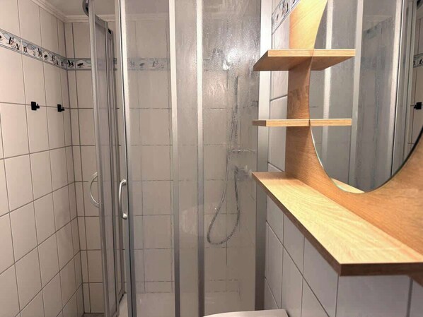 Un espace douche doté d’une porte en verre, d’une étagère en bois et d’un miroir.