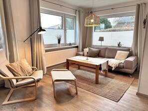 Een moderne woonkamer met een bank, fauteuil, salontafel en hanglamp.
