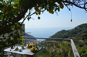 A balcony with a table set for a meal, overlooking a coastal landscape with terraced vineyards. - Apartment in Ravello (Ravello)