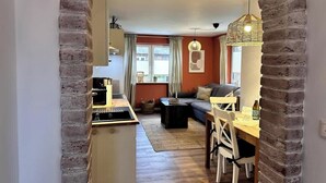 A living area with a sofa, dining table, and kitchen area with a brick archway. - Strandhütte direkt am Leuchtturm und Strand in SPO (Sankt Peter-Ording)