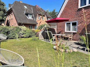 A residential property with a well-maintained lawn, a wooden deck, and a brick house with a sloped roof.
