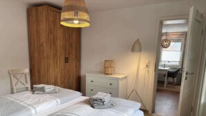 A bedroom with two beds, a wooden wardrobe, a bedside table with a lamp, and a view into the bathroom. - Wohnung am Strand in SPO mit Boxspringbett (Sankt Peter-Ording)