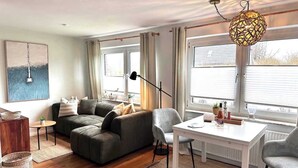 A modern living room with a sofa, a dining table, and a hanging light fixture. - Wohnung am Strand in SPO mit Boxspringbett (Sankt Peter-Ording)