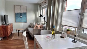 A modern living room with a white table, grey sofa, and a painting on the wall. - Wohnung am Strand in SPO mit Boxspringbett (Sankt Peter-Ording)