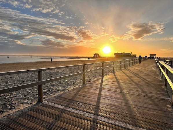 A wooden boardwalk leading to a beach with a sunset in the background.
