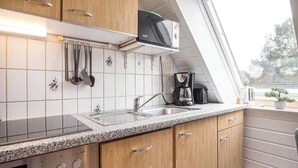A kitchen with wooden cabinets, a stainless steel sink, a microwave, and a coffee maker. - Helle Wohnung mit 2 Schlafzimmern (Sankt Peter-Ording)