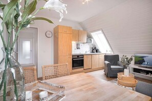Een moderne keuken met houten kastjes, een eethoek met rieten meubels, en een televisie in de woonkamer.