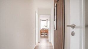 A hallway with a wooden floor, white walls, and a door with a metallic handle. - Helle Wohnung mit 2 Schlafzimmern (Sankt Peter-Ording)