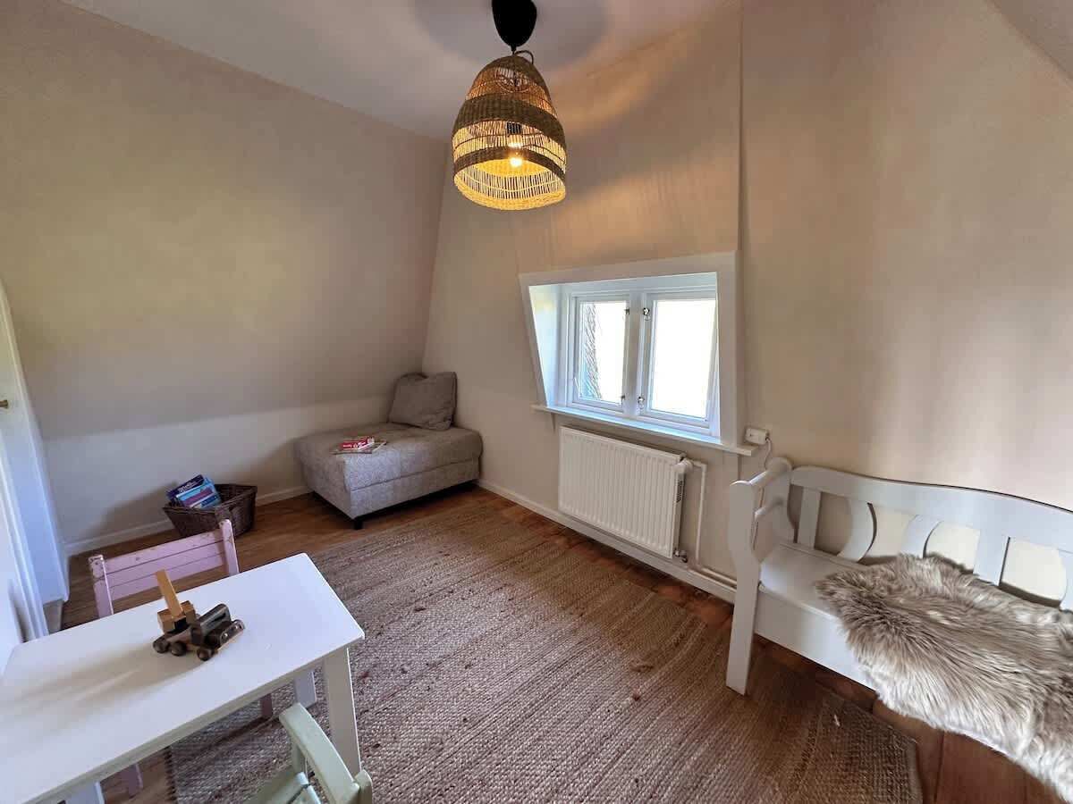 A cozy room with a white sofa, a small table with a toy, a wicker lamp, and a window with a view.