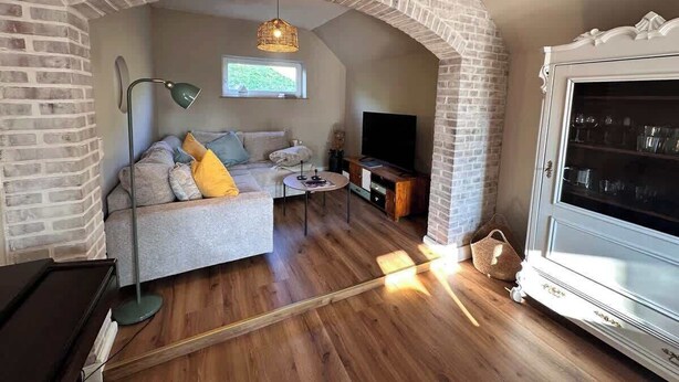 A cozy living room with a brick archway, a sofa with cushions, a coffee table, a TV, and a cabinet with glass doors.