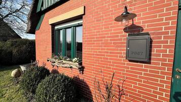 A red brick building with a green window, a mailbox, and a small garden area with plants and a rock.