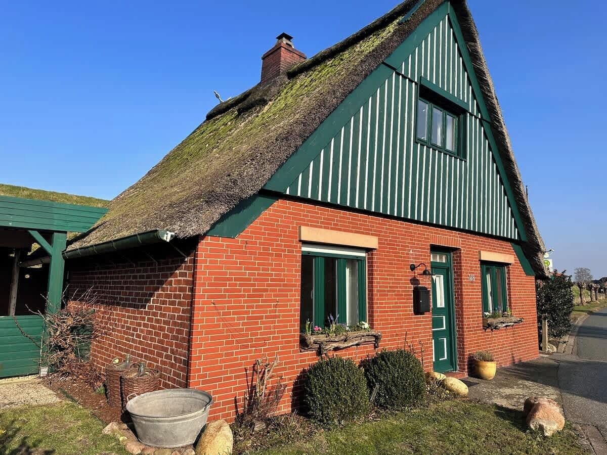 A traditional brick house with a thatched roof, green shutters, and a small front porch area.