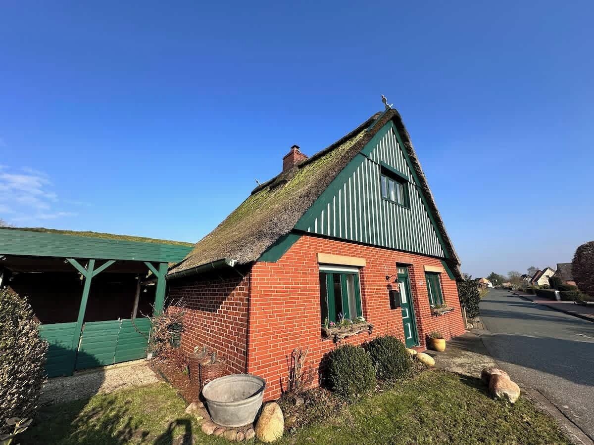 A traditional red brick house with a thatched roof and green trim.