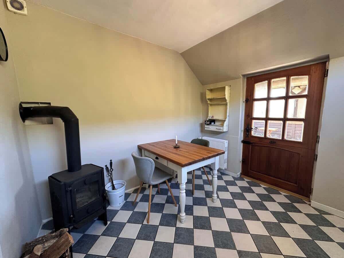 Ein Zimmer mit Schachbrettboden, einem Holztisch, einem Stuhl, einem schwarzen Herd und einer Tür mit Fenstern.