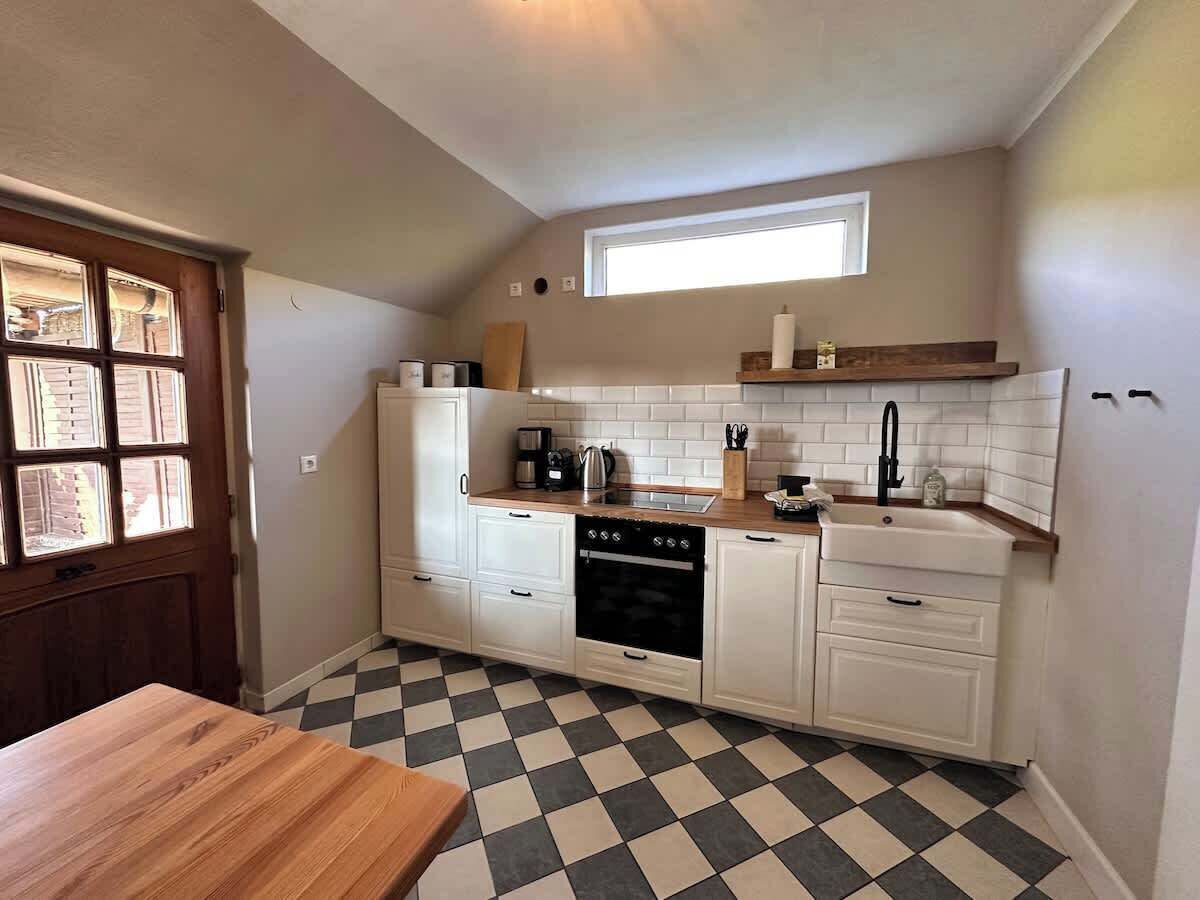 A compact kitchen with white cabinets, a black oven, a wooden countertop, and a checkered floor.