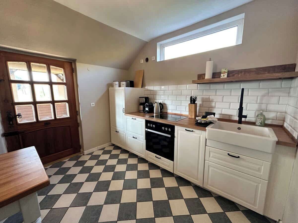 A kitchen with a checkered floor, white cabinets, a stove, and a window above the sink.