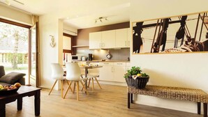 A modern kitchen with white cabinets, a dining area with a table and chairs, and a large window. - Zentrale Wohnung mit Terrasse & Boxspringbett (Sankt Peter-Ording)