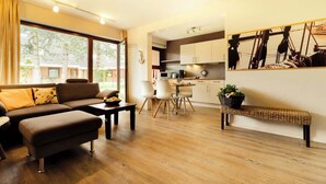 A modern living room with a sofa, ottoman, and dining area with chairs and a table. - Zentrale Wohnung mit Terrasse & Boxspringbett (Sankt Peter-Ording)