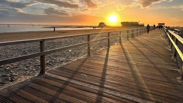 Un muelle de madera que conduce a una playa con un atardecer al fondo.