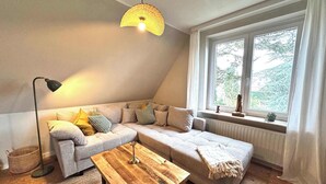 A cozy loft bedroom with a large window, a wooden coffee table, and a modern lamp. - Quiet, comfortable apartment near the beach (Sankt Peter-Ording)